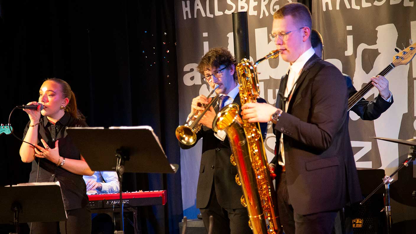 Sångare, saxofonist, trumpetist och basist spelar musik på scen.