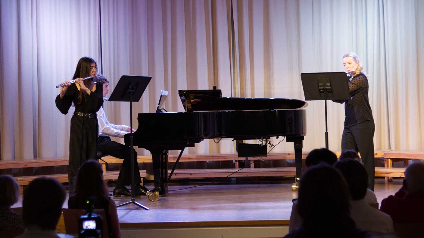 Två flöjtister och en pianist spelar musik på scen.