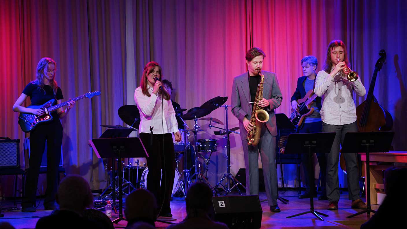 Sex personer spelar musik på scen i lila scenljus.