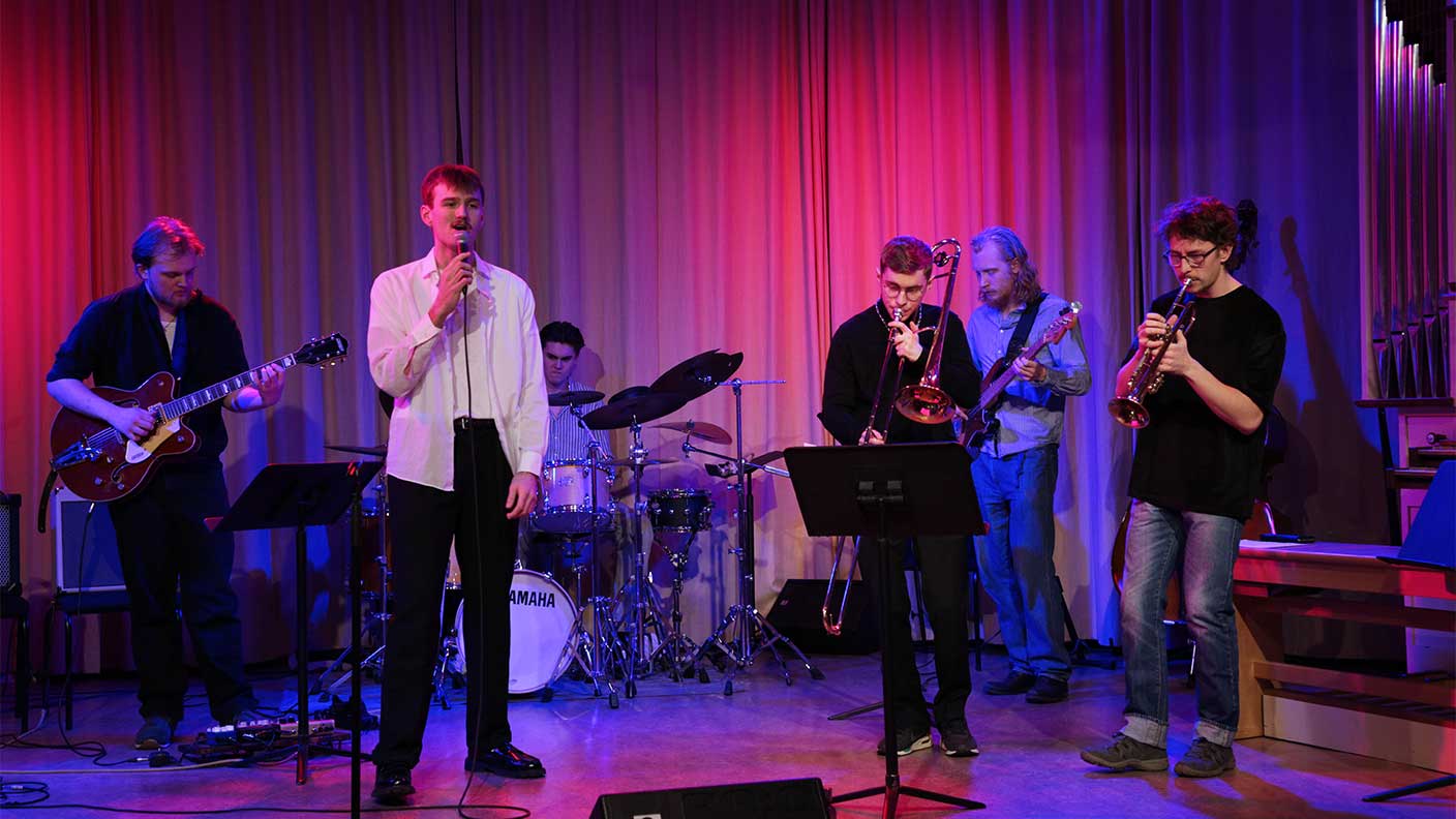 Sex personer spelar musik på scen i lila scenljus.