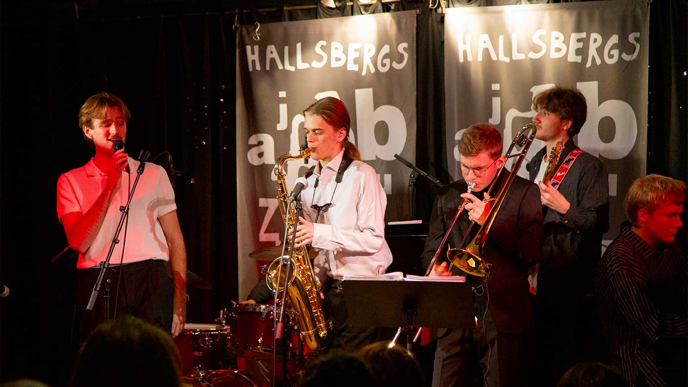 Fem unga män spelar saxofon, trumpet, elbas, piano och sjunger på scen.