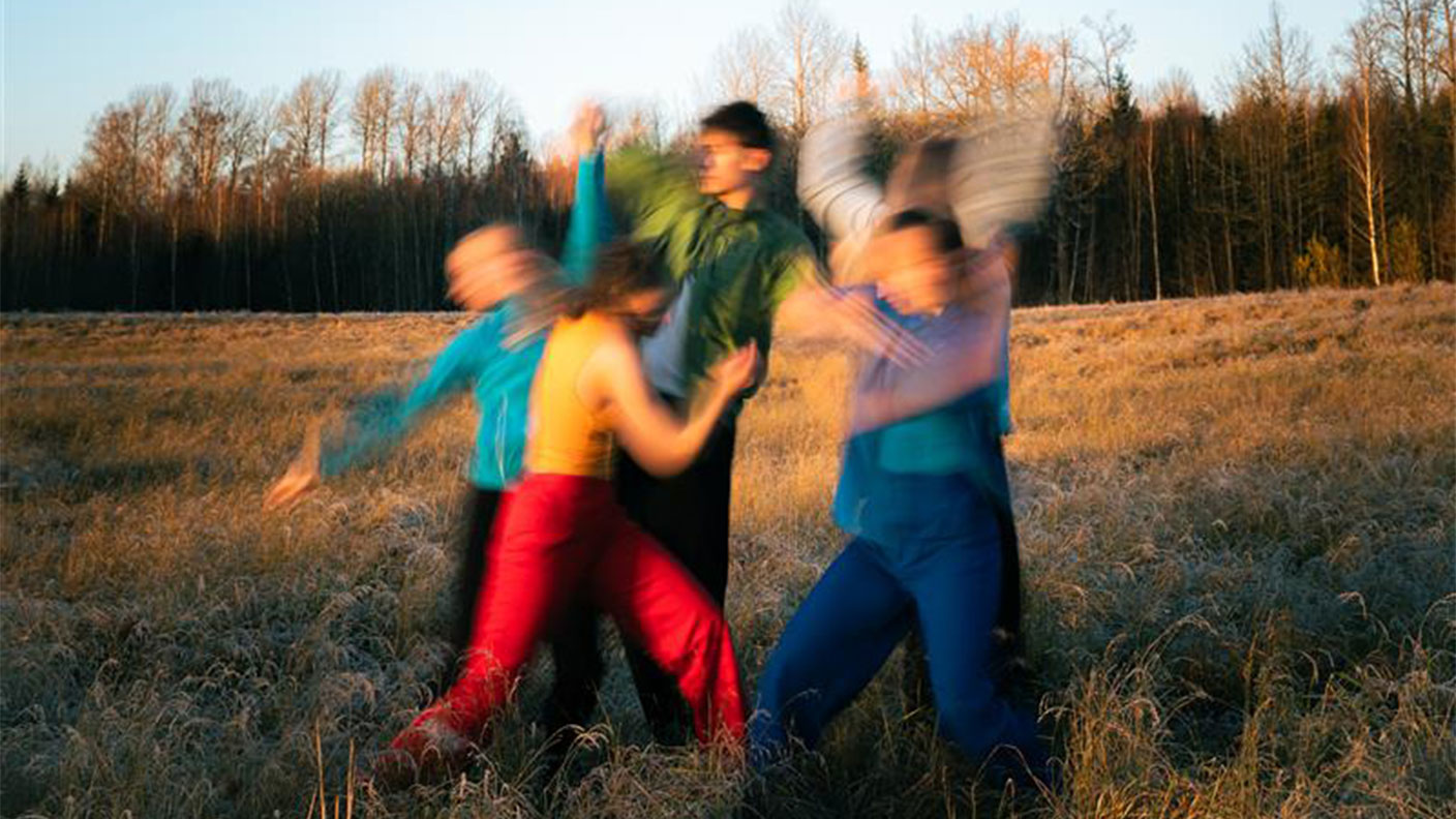 Fyra personer gör danskoreografi på äng, fotat så att rörelserna blir suddiga.