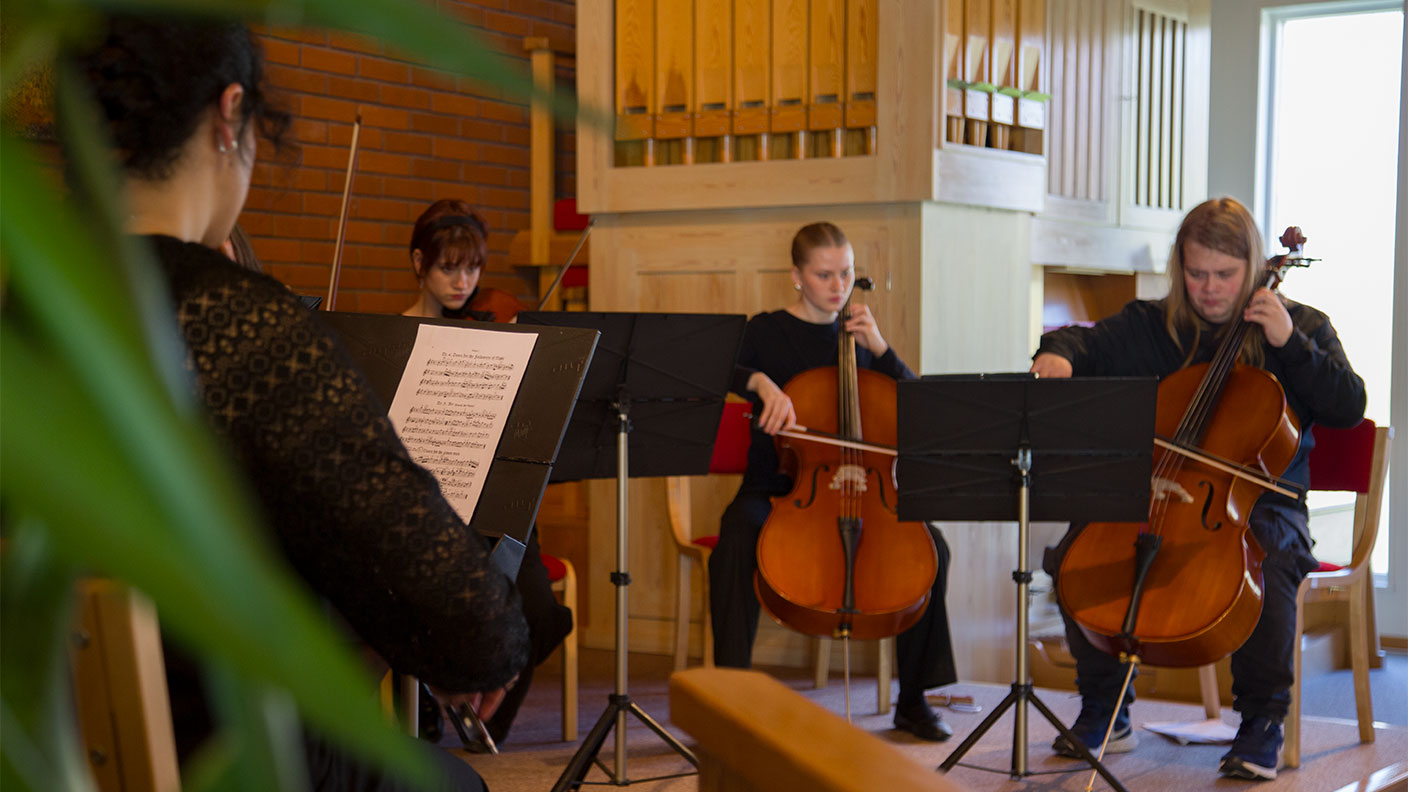 Tre personer spelar cello i kyrkmiljö.