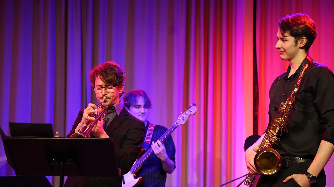 Tre killar på scen med trumpet, saxofon och bas.