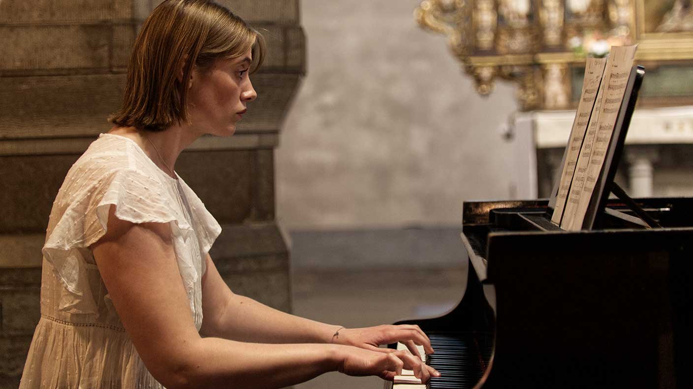 Kvinna med vit tunika spelar piano i kyrka.