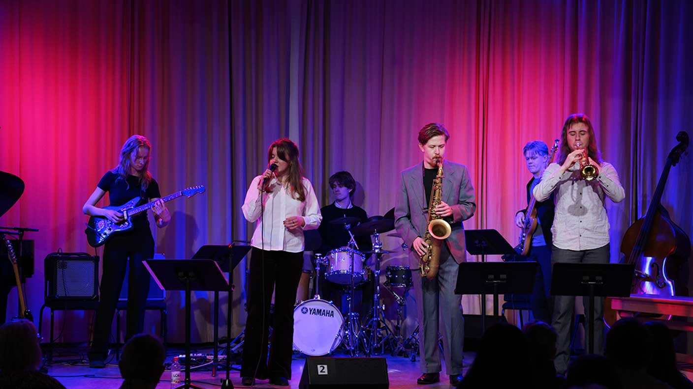 Fem unga vuxna spelar musik på scen i lila scenljus.