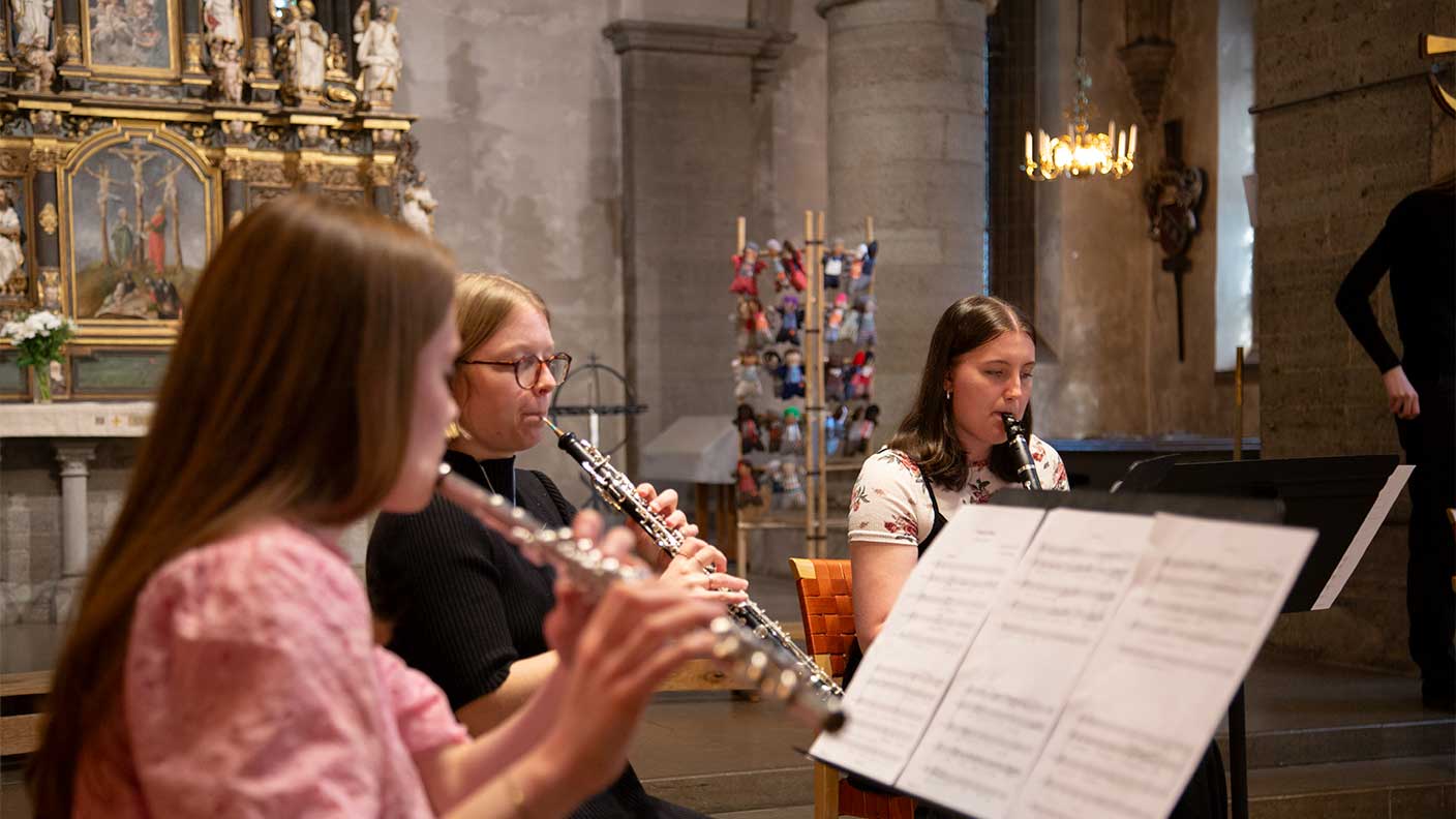 Tre kvinnor sitter och spelar träblåsinstrument i en kyrka.