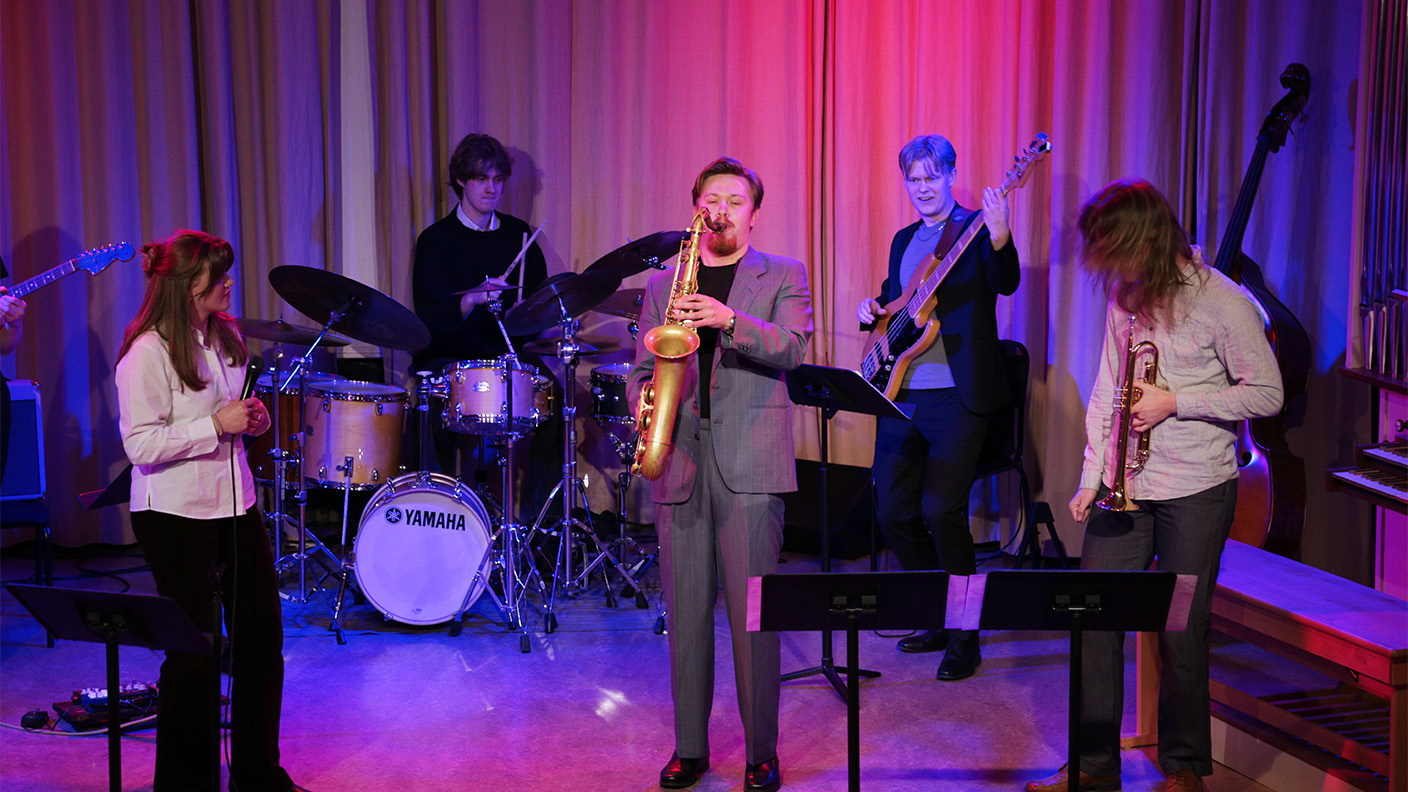 Ungdomar spelar musik på scen i lila scenljus.