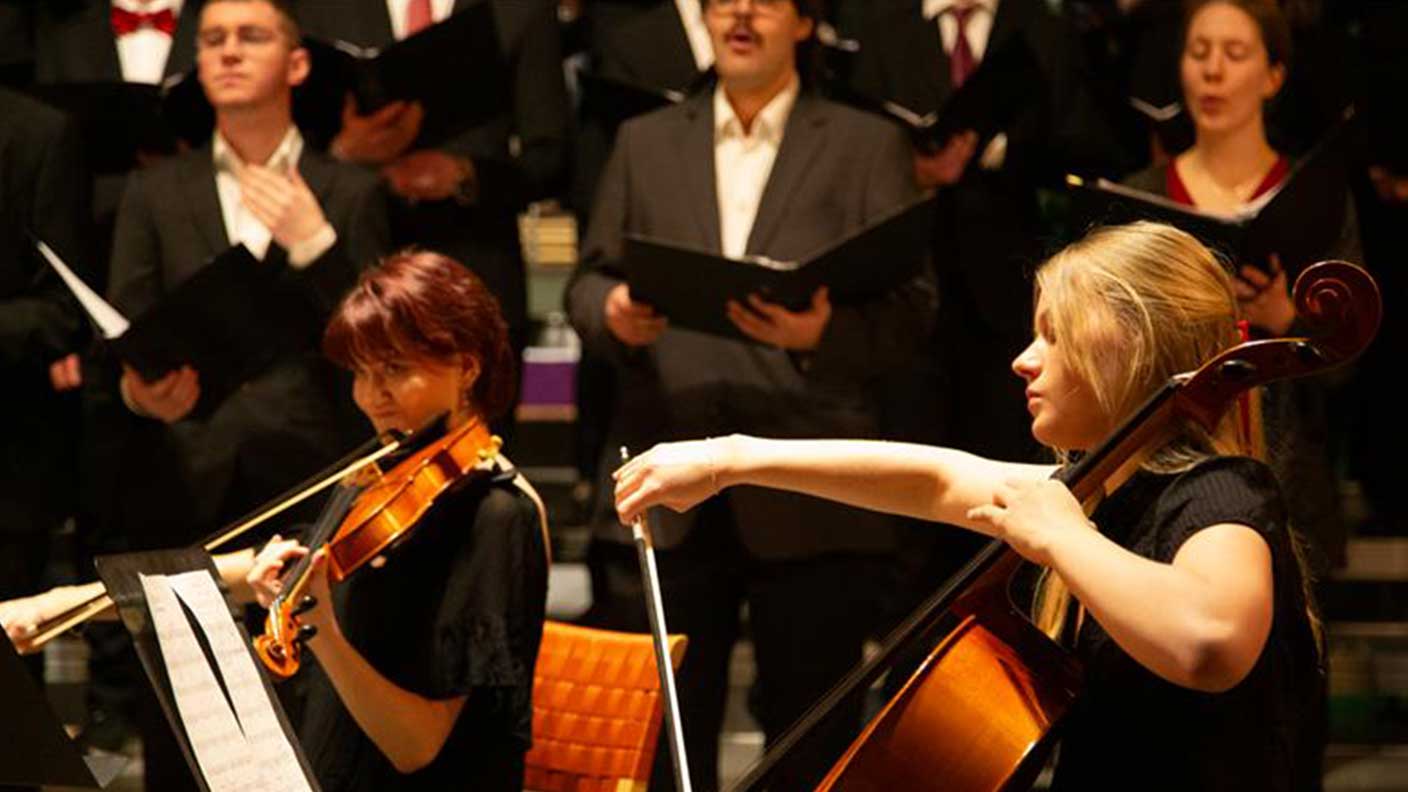 I förgrunden kvinnlig cellist och kvinnlig violinist. Kör i bakgrunden.