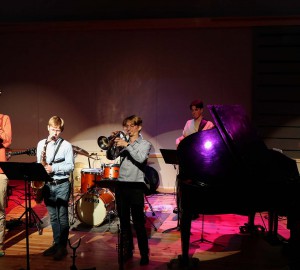En jazzensemble, inklusive flygel, spelar i en stor sal.