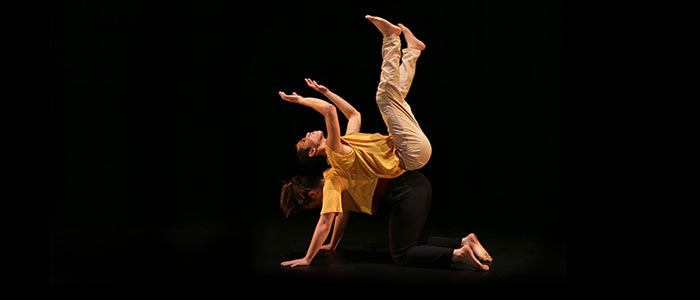 Två dansare balanserar på varandra. En står på alla fyra. En balanserar på den andra, liggande på rygg.