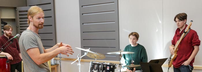 En lärare pratar med tre deltagare som spelar congas, trummor och bas.