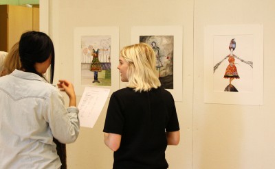 Tre personer tittar på teckningar som hänger på väggen.