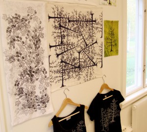 En samling tygtryck och två t-shirts hänger på en vägg.