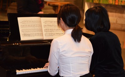 Två pianister vid ett piano. Ena i vit blus, andra i svart tröja.