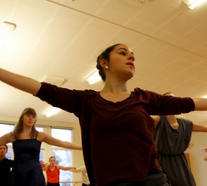 En dansare i halvfigur nära kameran, armarna utsträckta åt sidorna, huvudet vänt åt höger.