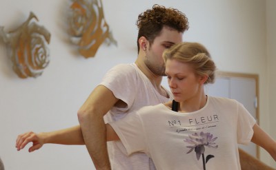 En dansare sträcker sin arm igenom bågen som en annan dansares arm bildar.