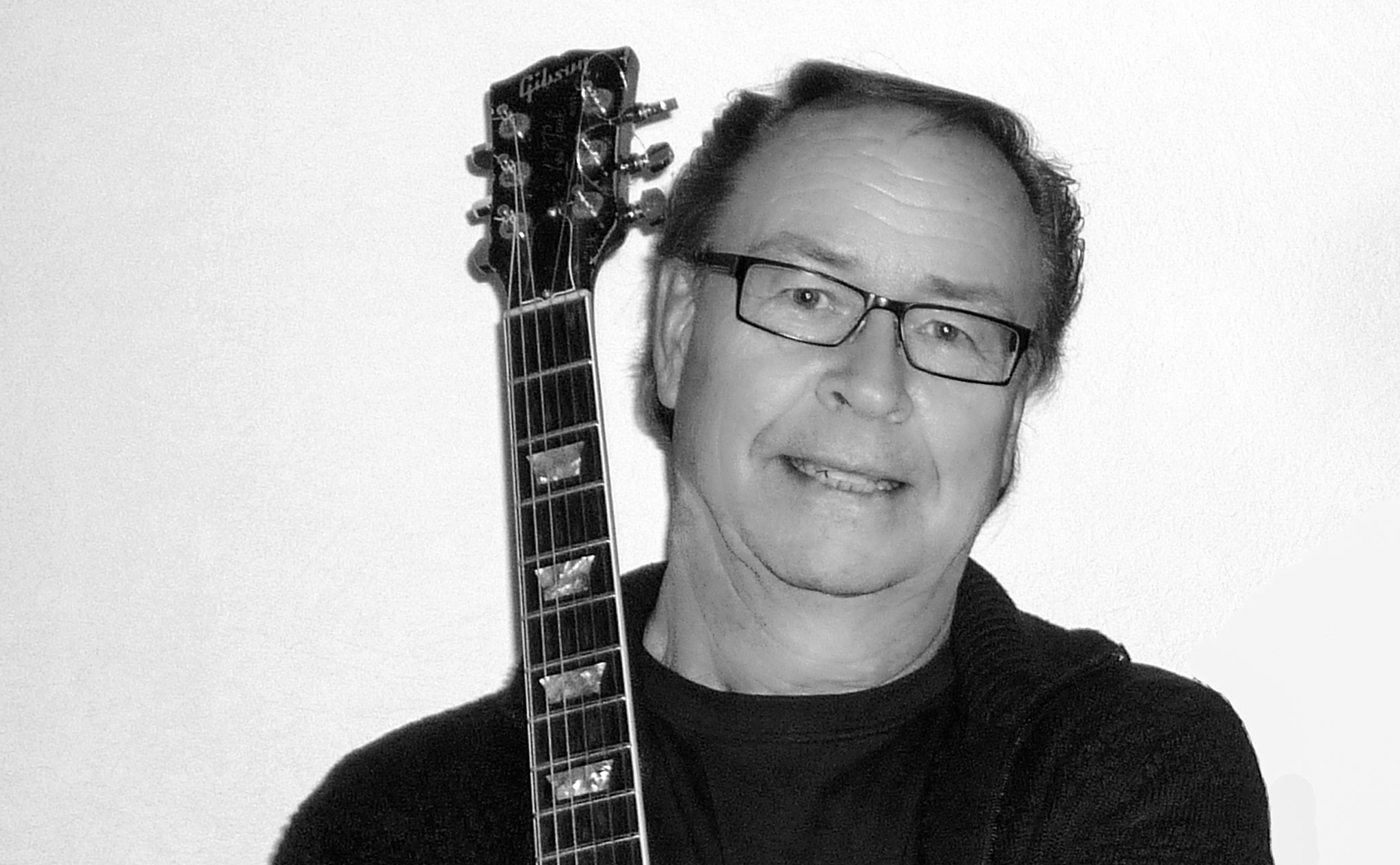 Porträttbild på Ewan Svensson med en gitarr mot axeln.