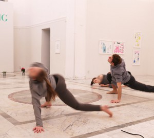 Två dansare med en hand och två fötter i golvet. Dom böjer kroppen uppåt. Det går fort, bilden är suddig.
