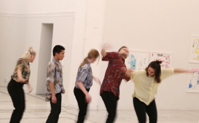 Fem dansare står på rad horisontellt över bilden. De skakar ryckigt med sina kroppar.