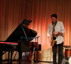 Saxofonist spelar solo. Till vänster en deltagare på keyboard och i bakgrunden en trummis.