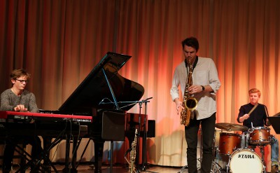 Saxofonist spelar solo. Till vänster en deltagare på keyboard och i bakgrunden en trummis.