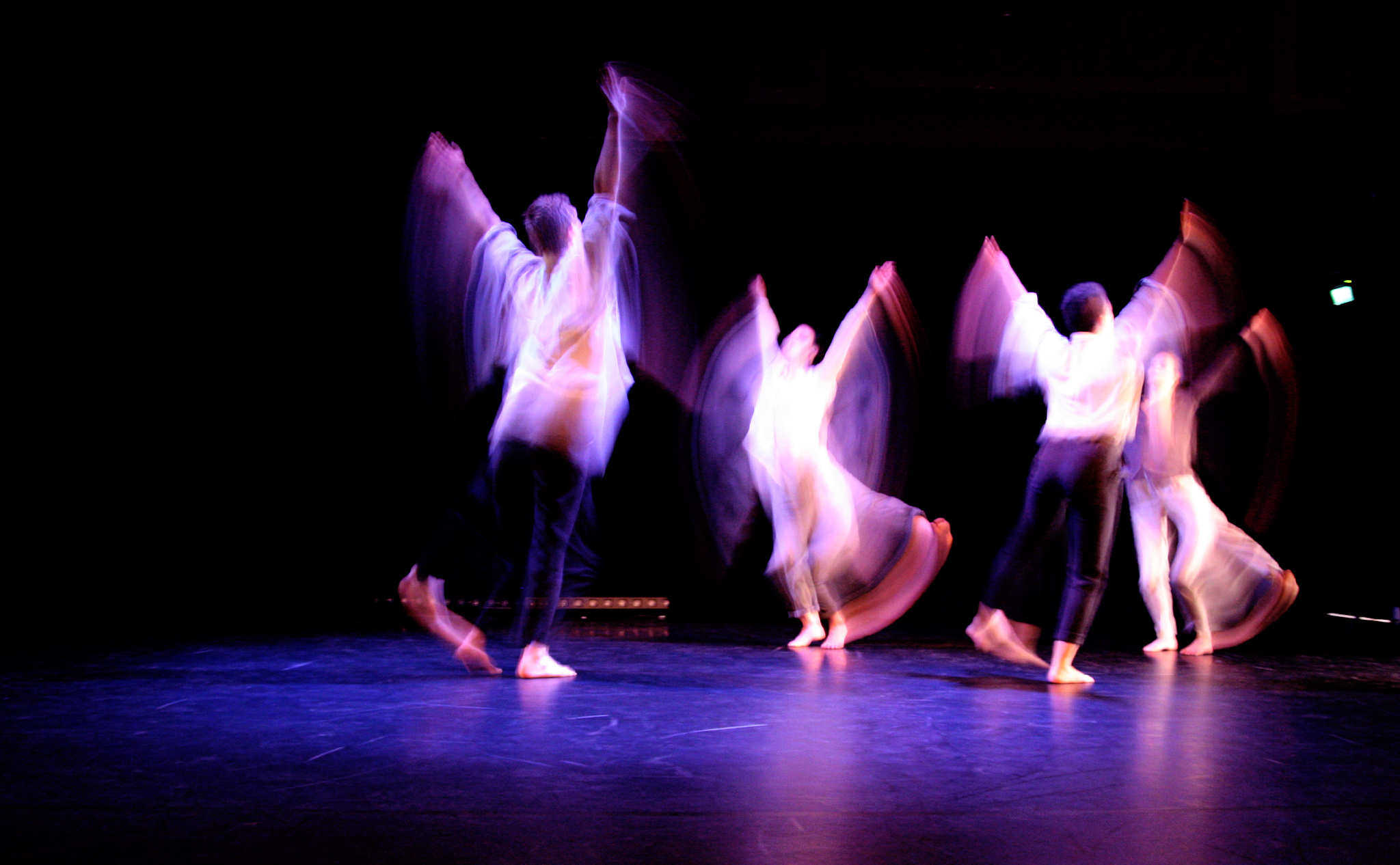 Tre dansare på scen i lila ljus. Dom rör sig snabbt och är suddiga konturer.