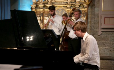 Pianist i förgrunden och delar av en jazzensemble i bakgrunden.