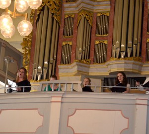 Sångare på en kyrkobalkong, framför en orgel.