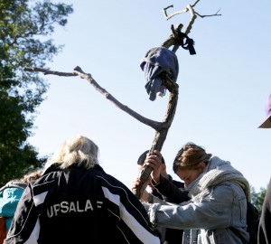 Deltagare i förgrunden håller upp en lång trädstam som dom virat tyg omkring.