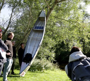 Flera deltagare samlade runt en kanot som ställts på högkant mot ett träd.