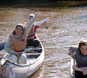 Två deltagare i en kanot vinkar till kameran.