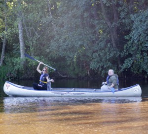 Två deltagare i en kanot, vinkar med sina paddlar.