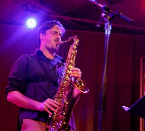 En saxofonist spelar solo, bakom huvudet lyser en stark scenlampa.