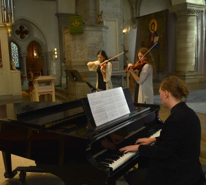 Konsert i kyrka. I förgrunden en pianist vid flyger. I bakgrunden blåsinstrument.