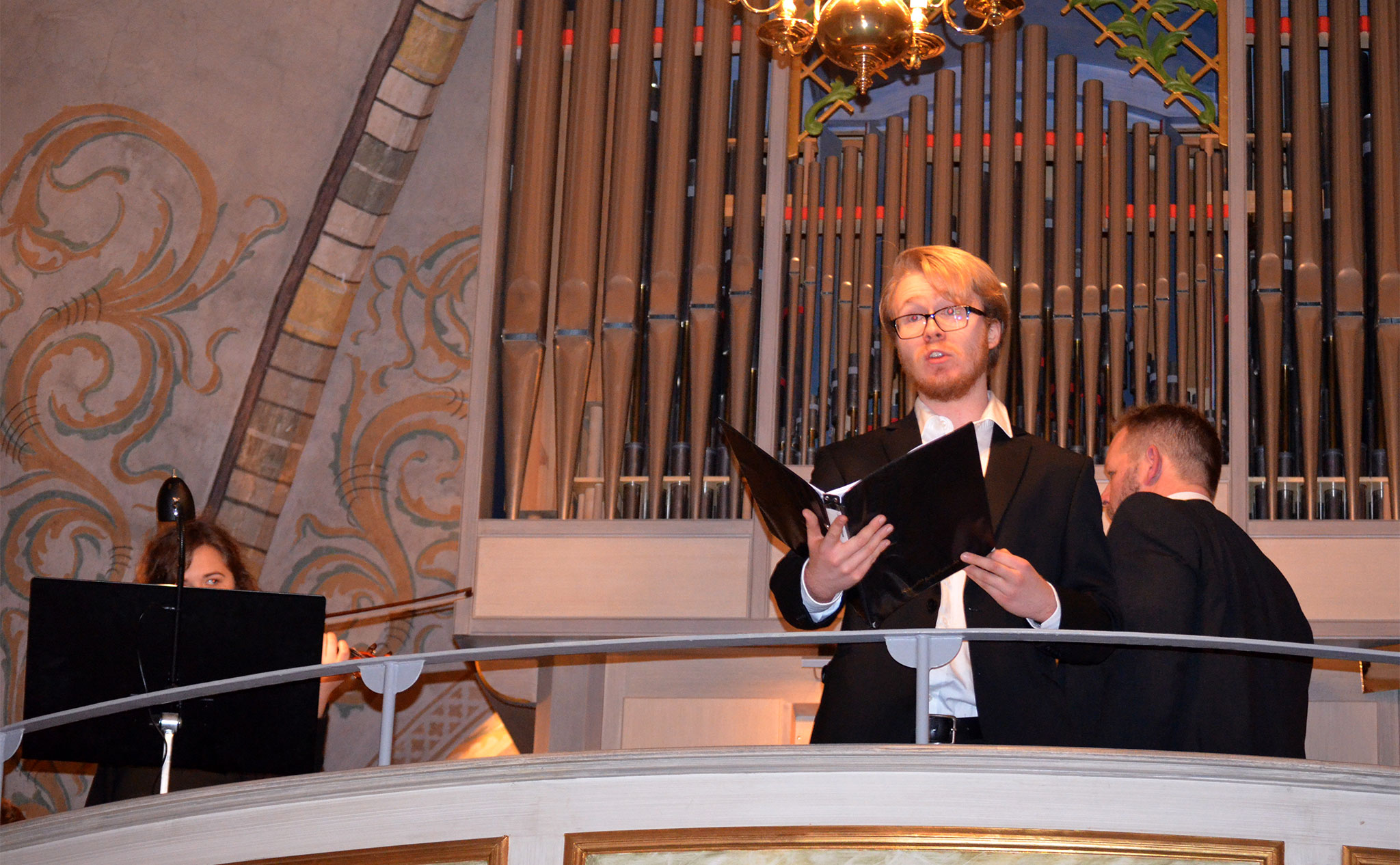 Sångare på balkong i kyrka. Orgel i bakgrunden.