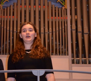 Sångerska på balkong i kyrka. Orgel i bakgrunden.