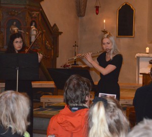 Två deltagare spelar flöjt respektive fiol framför publik i en kyrka.