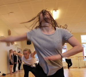 Dansare i förgrunden med huvudet bakåtkastat och håret för ansiktet.