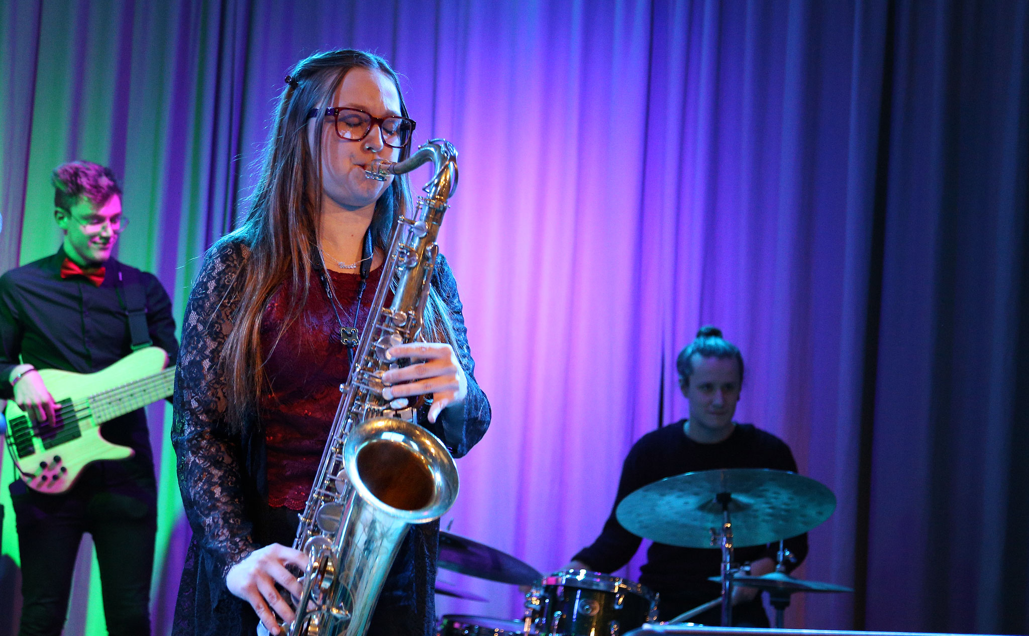 Konsertbild, i förgrunden en deltagare som spelar saxofon. I bakgrunden basist och trummis.