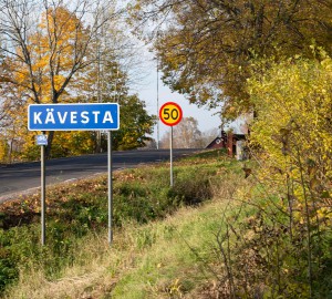 I förgrunden en blå vägskylt med texten Kävesta. Bakom den en röd och gul hastighetsskylt med texten 50.
