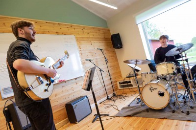 En gitarrist och en trummis spelar tillsammans i ett ljust övningsrum.
