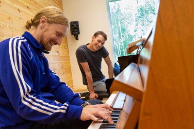 En lärare visar hur man spelar något på piano. Läraren och deltagaren skrattar.