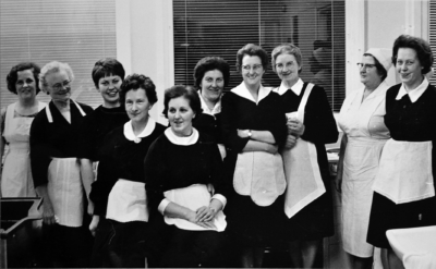Gruppfoto med 10 kokerskor. Alla utom en klädda i svarta klänningar och vita förkläden. En av dem är helt klädd i vitt.