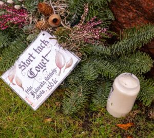 På en krans med barr, kottar och andra växter ligger ett laminerat kort där det står "Stort tack Coyet. Från Kävesta folkhögskola, 150 år".