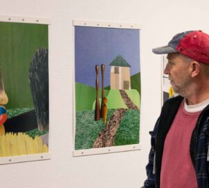 En man i röd keps står och tittar på två kollage som liknar målningar.